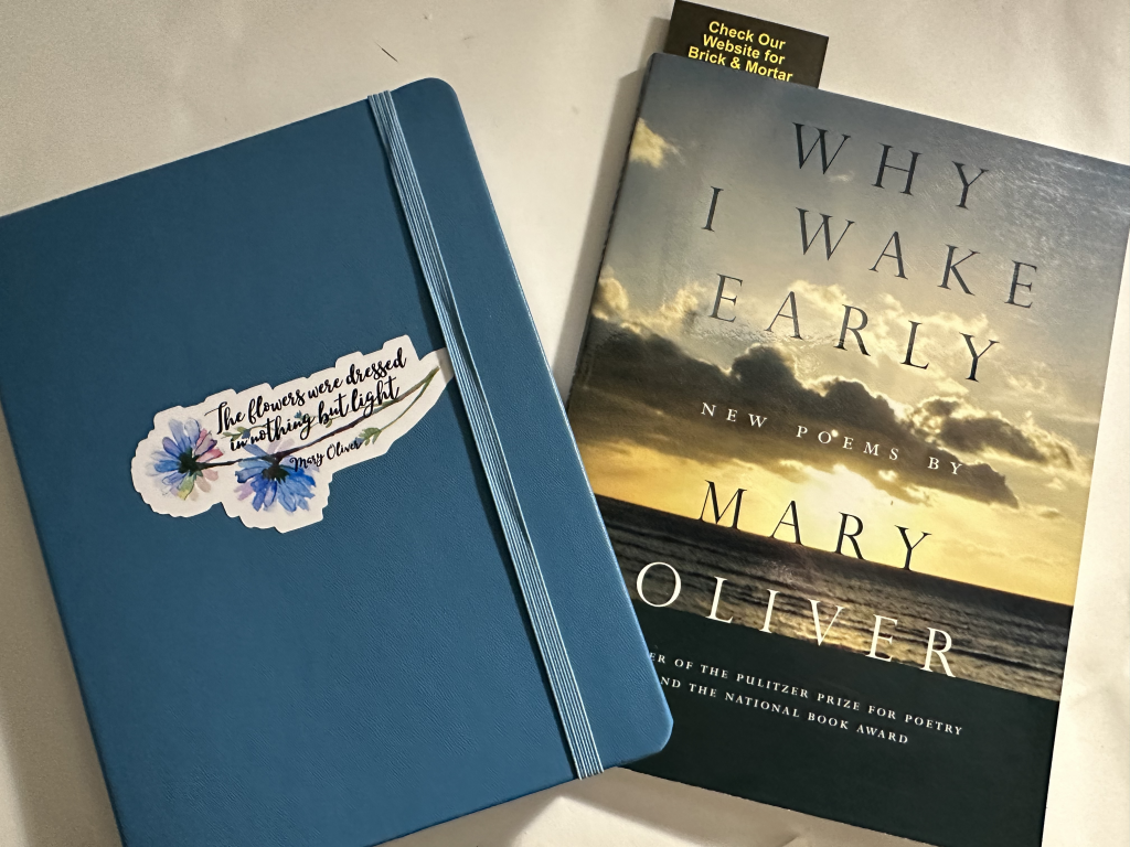 Picture of a blue notebook with a Mary Oliver quote that says, "The flowers were dressed in nothing but light." The notebook is next to a copy of the Mary Oliver poetry collection, WHY I WAKE EARLY. 